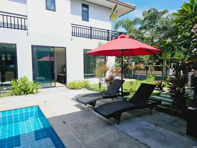 two chairs and a red umbrella next to a swimming pool at KRAAM VILLAS in Thalang