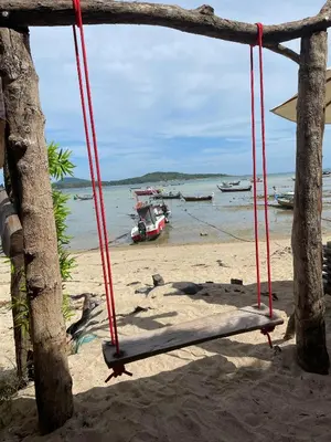 a swing on a beach with boats in the water at Villa KEWALYN in Chalong