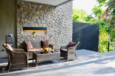 a patio with chairs and a table and a stone wall at Villa Papaya @ Kamala Beach in Kamala Beach