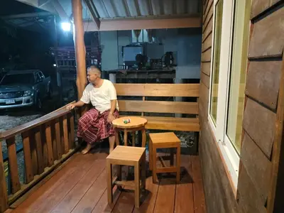 a man sitting on a porch with a table at ฟาดิลบังกะโล Fadel bungalow in Ban Lo Pa Ret