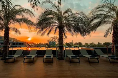 a deck with chairs and palm trees at sunset at Citygate Condo Kamala Phuket in Kamala Beach