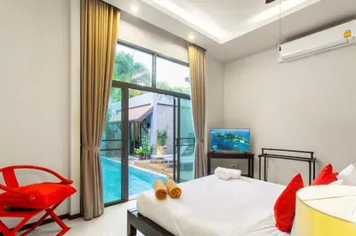 a bedroom with a bed and a red chair and a tv at Stylish 3BR Pool Villa Onyx H4, Gated Residence, Near Rawai & Naiharn Beach in Rawai Beach