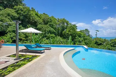 a swimming pool with two chairs and an umbrella at Kata Beach Luxury Condo - Spacious - Exquisitely Furnished - 6min walk to beach - 2025 Booking Traveller Award Winner in Kata Beach