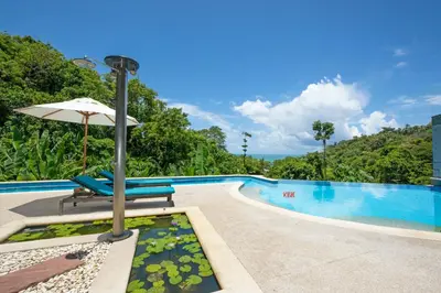 a swimming pool with an umbrella and chairs next to a pool at Kata Beach Luxury Condo - Spacious - Exquisitely Furnished - 6min walk to beach - 2025 Booking Traveller Award Winner in Kata Beach