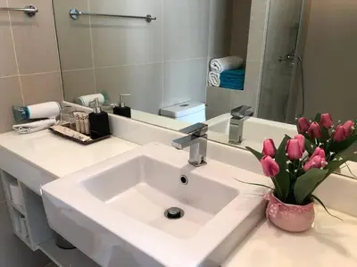 a bathroom with a sink with a vase of pink flowers at Aristo Resort Surin Beach M06 in Phuket Town