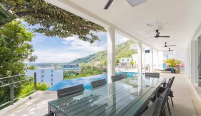 an outdoor patio with a glass table and chairs at Villa Ginborn 5 bedroom Pool Villa with Sea View in Kata Beach in Kata Beach