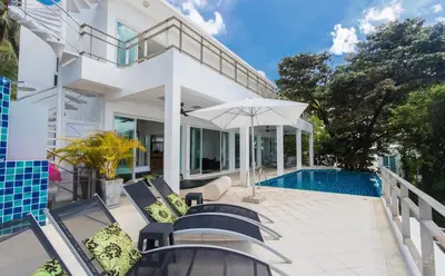 a white house with a swimming pool and chairs and an umbrella at Villa Ginborn 5 bedroom Pool Villa with Sea View in Kata Beach in Kata Beach