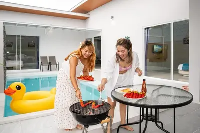 two women cooking food on a grill next to a pool at Sasi Pool Villa Phuket in Rawai Beach