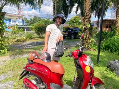 a man is standing next to a red scooter at Lay Back Villa C2 with Kitchen & High speed Internet in Krabi town