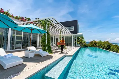 a woman standing next to a swimming pool next to a house at Phuket 4-6 Bedroom Seaview Villa Infinity 25mPool In-Villa Dining & Butler Gym in Thalang