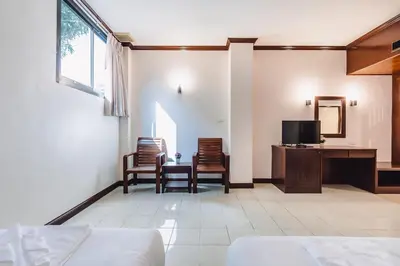 a room with a bed and chairs and a tv at Bauman-Ville Hotel Patong in Patong Beach