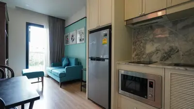a kitchen with a refrigerator and a living room with a table at DLUX Condominium Chalong Phuket in Ban Klang
