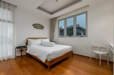 a white bedroom with a bed and two windows at WEG Elite Beachfront in Phuket Town