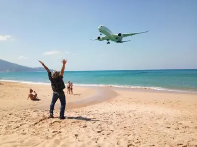 a person standing on a beach with an airplane flying over the ocean at Haru Inn Airport in Ban Bo Han