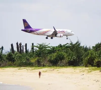 a plane flying over a beach with a man standing on the sand at Haru Inn Airport in Ban Bo Han