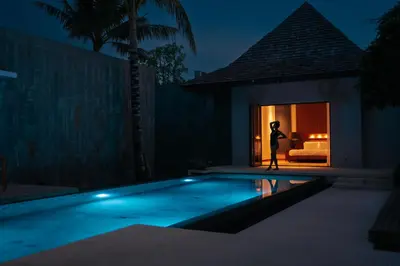 a person standing next to a swimming pool at night at Allure Villa in Bangtao in Ban Pak Lak