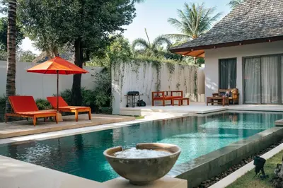 a swimming pool with chairs and an umbrella next to a house at Allure Villa in Bangtao in Ban Pak Lak