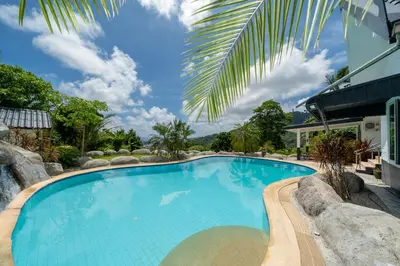 a swimming pool in a resort with a palm tree at Villa Olympus Ocean Vista Kata Beach in Kata Beach