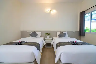 two beds in a room with a window at Puean Chang Resort Phuket in Thalang