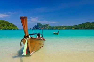 a boat sitting in the water on a beach at Phuttachot Resort in Phi Phi Don