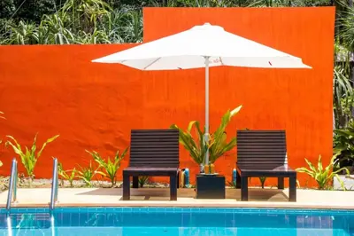 two chairs and an umbrella next to a swimming pool at Natai House Resort นาใต้เฮ้าส์ รีสอร์ท in Natai Beach
