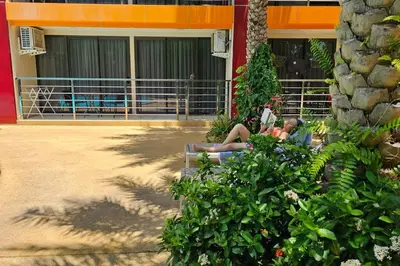two people sitting on a bench in front of a building at Новая квартира с выходом к бассейну in Mai Khao Beach