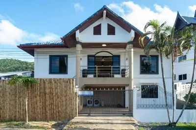 a white house with a fence and a palm tree at Golden Sands Villa only 15 minutes walk to beach in Surin Beach