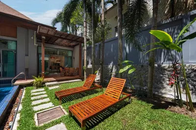 two wooden chairs sitting in the grass next to a house at Villa Laut 3BR Private Pool 10 min to Nai Harn in Rawai Beach