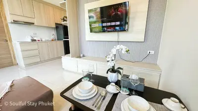 a living room with a table and a tv on the wall at Soulful Stay Phuket -Distant Seaview and Mountain View Retreat, Patong in Patong Beach