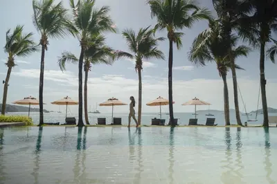 a woman walking by a swimming pool with palm trees at Bandara Pool Villas, Phuket in Panwa Beach
