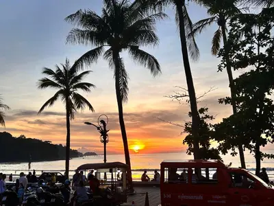 a sunset on a beach with palm trees and people at The Viva Patong Condo - 1Bdr - 35sqm Studio - Patong Hills in Patong Beach