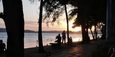 two people sitting on a bench on the beach at sunset at By the Sea Apartment Hotel in Krabi town