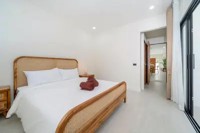 a bedroom with a white bed with a brown hat on it at Brand New 4BR Balinese Style Pool Villa Kaia just 5 min drive from NaiHarn Beach in Rawai Beach