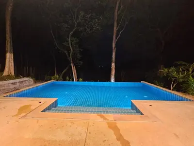 a blue swimming pool at night with trees in the background at Beachfront villa in Rawai in Phuket Town