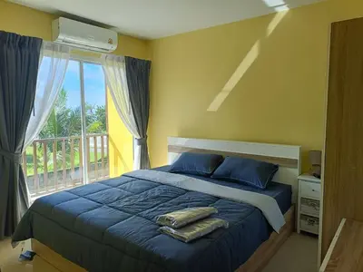 a bedroom with a bed with blue pillows and a balcony at Yellow house in Ban Saiyuan (1)