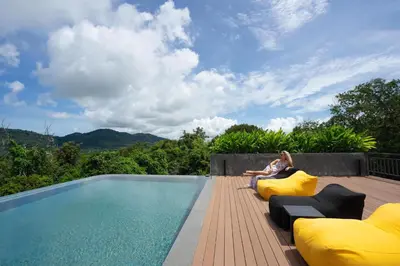 a woman sitting on pillows next to a swimming pool at Spacious Pool View 1BR Apartment in Utopia Naiharn Residence near Beach, UTN D604 in Rawai Beach