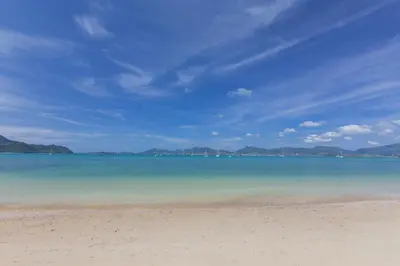 a beach with the ocean and mountains in the background at X10 Seaview Suites at Panwa Beach in Panwa Beach