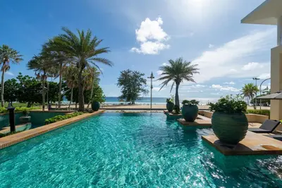 a swimming pool with palm trees and the ocean at Karon Beachfront Apartment 703 in Karon Beach