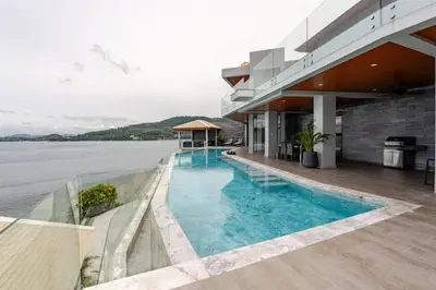 a building with a swimming pool next to the water at Cape Sienna Villa 4-Oceanfront 5-Bedroom Luxury Villa with 22 m Infinity Pool in Kamala Beach