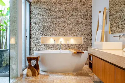 a bathroom with a large tub and a stone wall at Stylish Pool Villa Tropical Hideaway in Ban Phru Champa