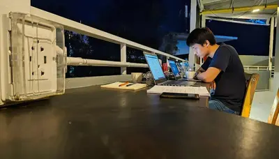 a man sitting at a table with a laptop computer at Friends Hostel - Phuket Airport in Nai Yang Beach