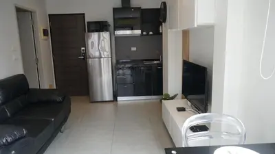 a living room with a black couch and a kitchen at Island Escape 1BR T1-206 in Chalong