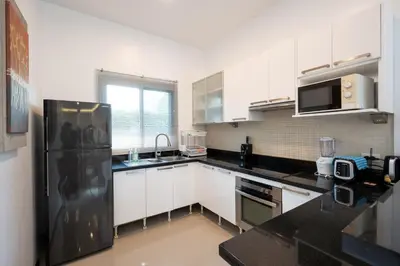 a kitchen with white cabinets and a black refrigerator at Tranquil 3 Bedroom Garden Pool Villa in Laguna Phuket