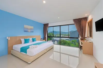a bedroom with a large bed and a large window at De Blue Sea Rawai Hotel in Ban Saiyuan (1)