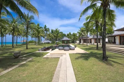 a garden with palm trees in front of a resort at Villa Ananda at Jivana Beach Villas in Pilai Beach