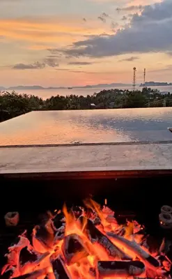 a fire burns in front of a body of water at Krabi Glass House Sea View Villa in Tab Kaek Beach