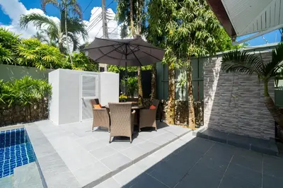 a patio with chairs and an umbrella next to a pool at Sanook villas Nai Harn beach in Rawai Beach