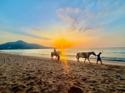 three people riding horses on the beach at sunset at TN KAMALA Room For Rent in Kamala Beach