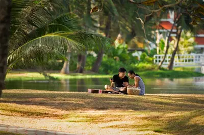 two people sitting on the grass near a body of water at 5 bdr Pool Villa Bang Tao Beach in Laguna Phuket