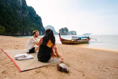 a man and woman sitting on a beach with a boat at Bulan Anda Resort in Ban Hua Laem